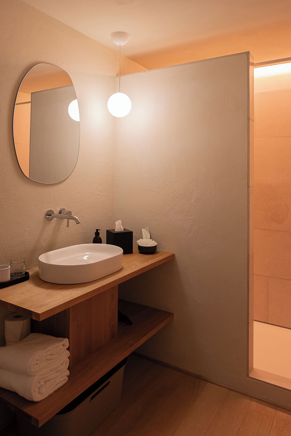 Een moderne badkamer met een ronde spiegel, een wit wastafelmeubel en een houten kast.