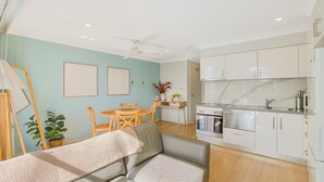 A compact kitchen with modern appliances, a dining area with a table and chairs, and a cozy seating area with a sofa. - Kirra On The Beach Apartments Unit 304 WIFI INCLUDED (Coolangatta)
