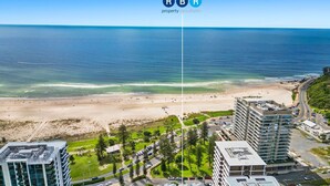 A coastal view with a beach, a road, and modern buildings. - Kirra On The Beach Apartments Unit 304 WIFI INCLUDED (Coolangatta)