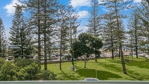 A parking lot with trees, a grassy area, and a road with vehicles. - Kirra On The Beach Apartments Unit 304 WIFI INCLUDED (Coolangatta)