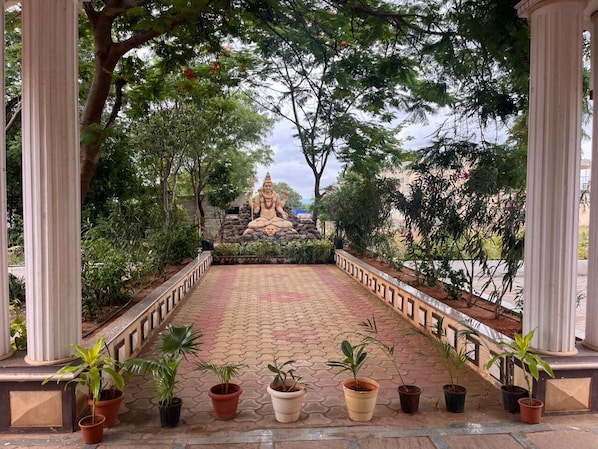 A pathway leading to a statue surrounded by trees and potted plants.