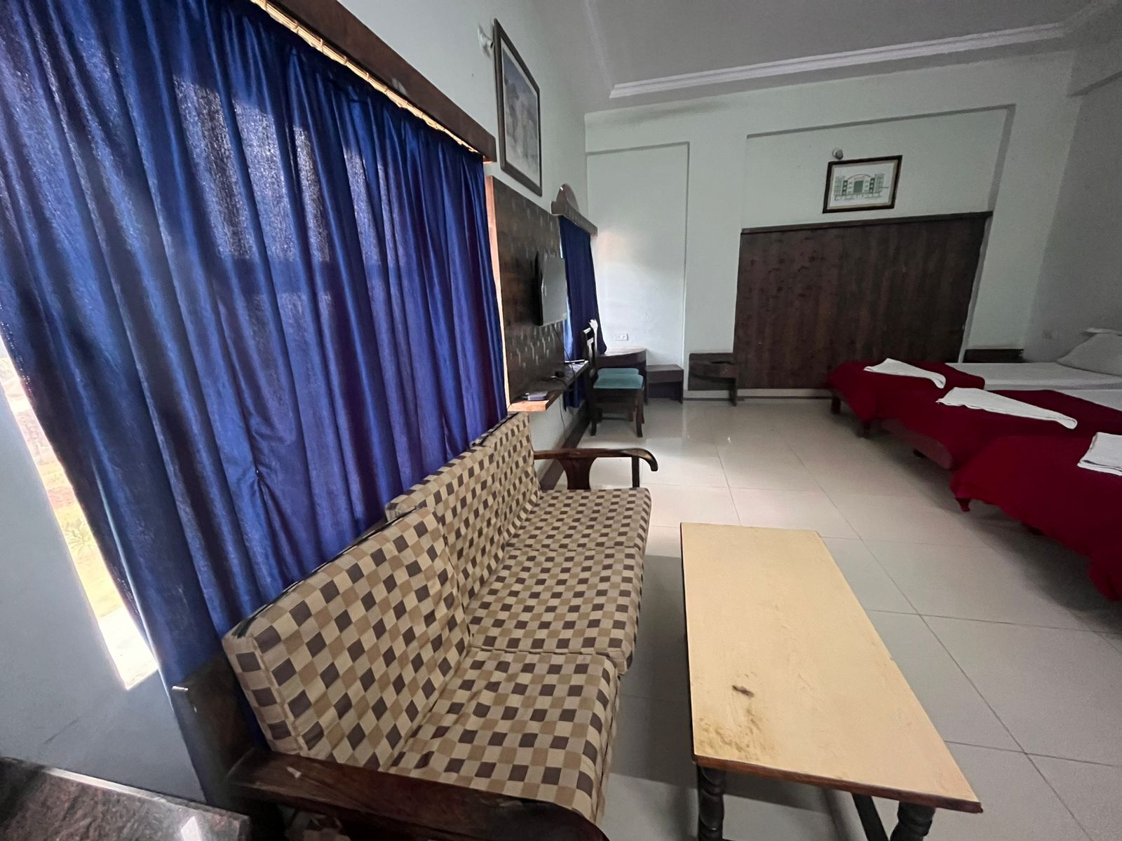 Una habitación con un sofá a cuadros, una mesa de madera y una cama con ropa de cama roja.