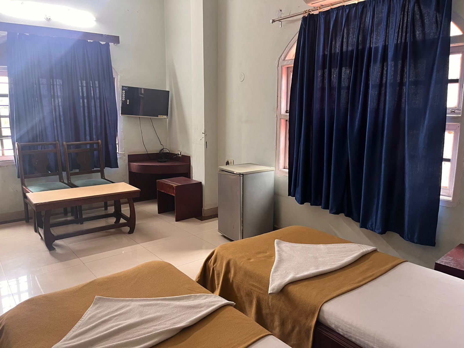 Une chambre avec deux lits, un bureau, une chaise, une petite table, une télévision et une fenêtre avec des rideaux.