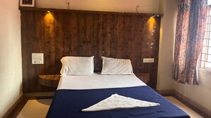 A bedroom with a wooden headboard, a bed with white linens, a blue bedspread, and a window with patterned curtains.