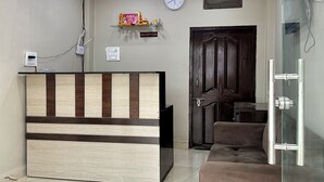 A reception area with a reception desk, a clock, a ceiling fan, and a sofa. - Hotel JMD 11 (Indore)