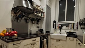 A modern kitchen with white cabinets, a stainless steel range hood, a built-in oven, and a window above the sink.