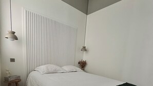 A bedroom with a bed, wooden floor, white walls, and a ceiling fan.