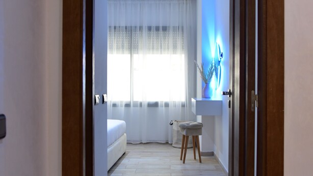 A hallway leading to a bedroom with a bed, a small table, and a chair.