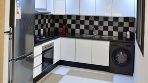 A modern kitchen with white cabinets, a black and white checkered backsplash, a stainless steel refrigerator, a gas stove, a washing machine, and a marble floor.