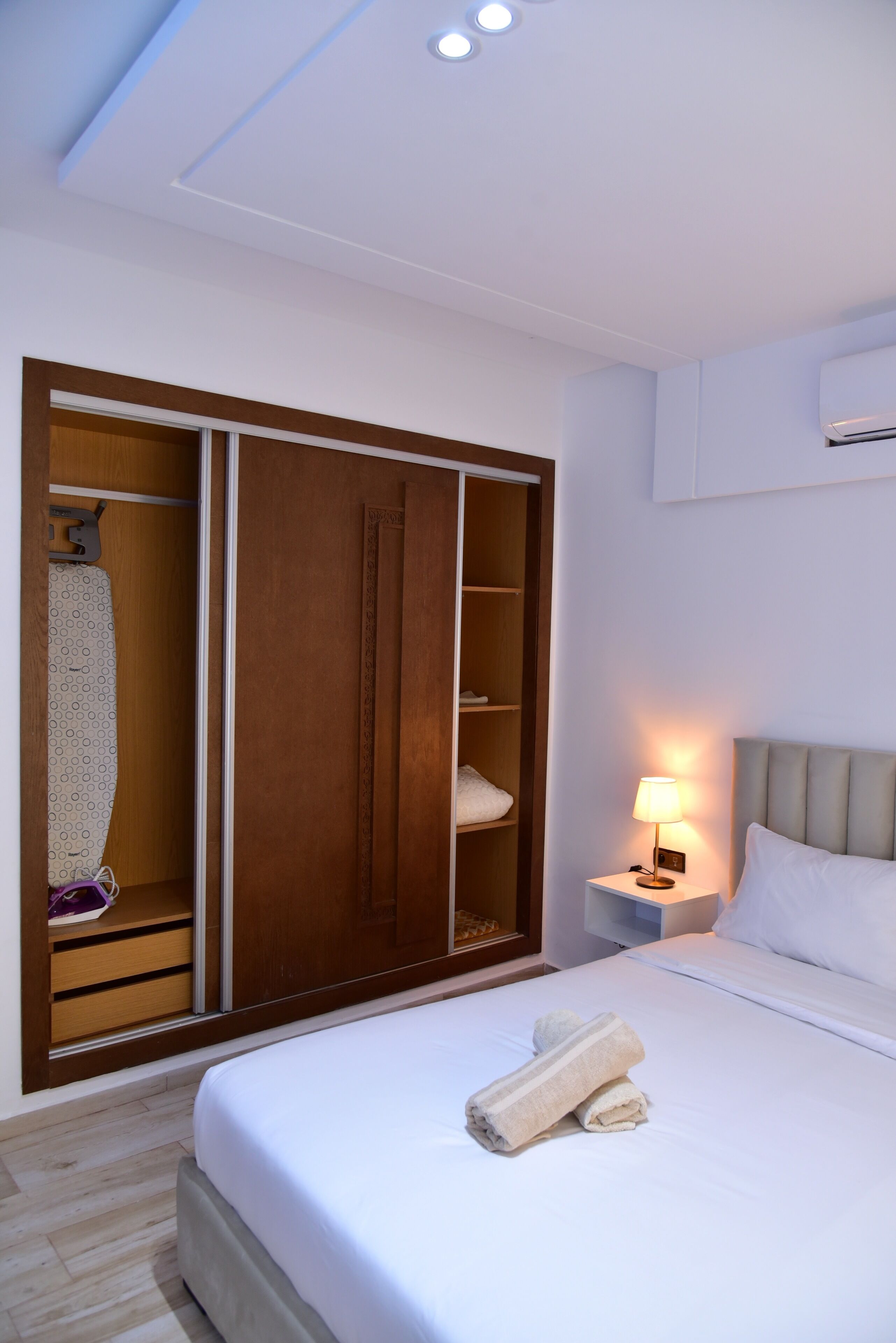 Una habitación de hotel con cama, mesita de noche con lámpara, armario y luz en el techo.