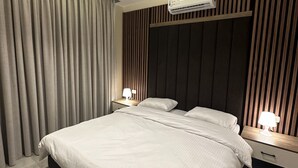 Ein modernes Schlafzimmer mit einem großen Bett, zwei Nachttischen mit Lampen, einer Decken-Klimaanlage und einem Fenster mit Vorhängen.
