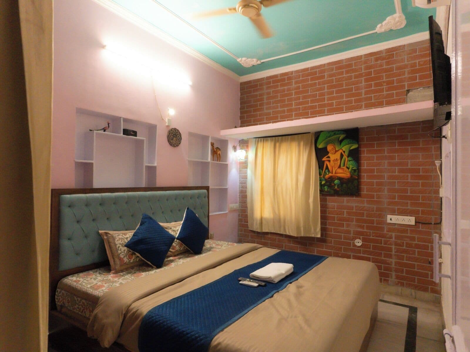 A hotel room with a bed, a ceiling fan, a brick wall, and a painting.