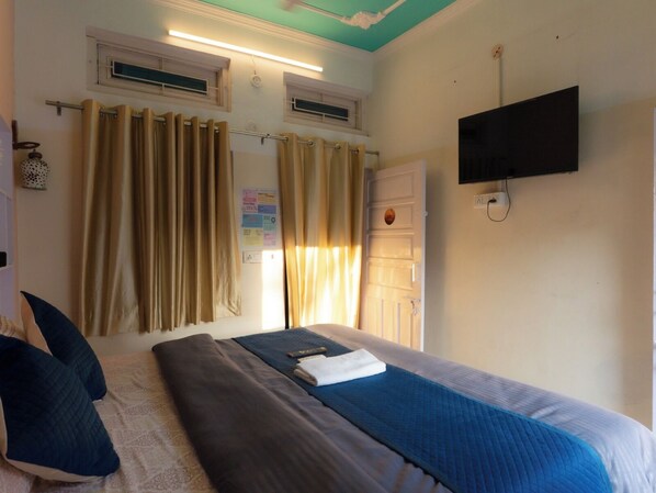A hotel room with a bed, curtains, a television, and a window with curtains. - The Pink Chapter Hostel, Jaipur (Jaipur)