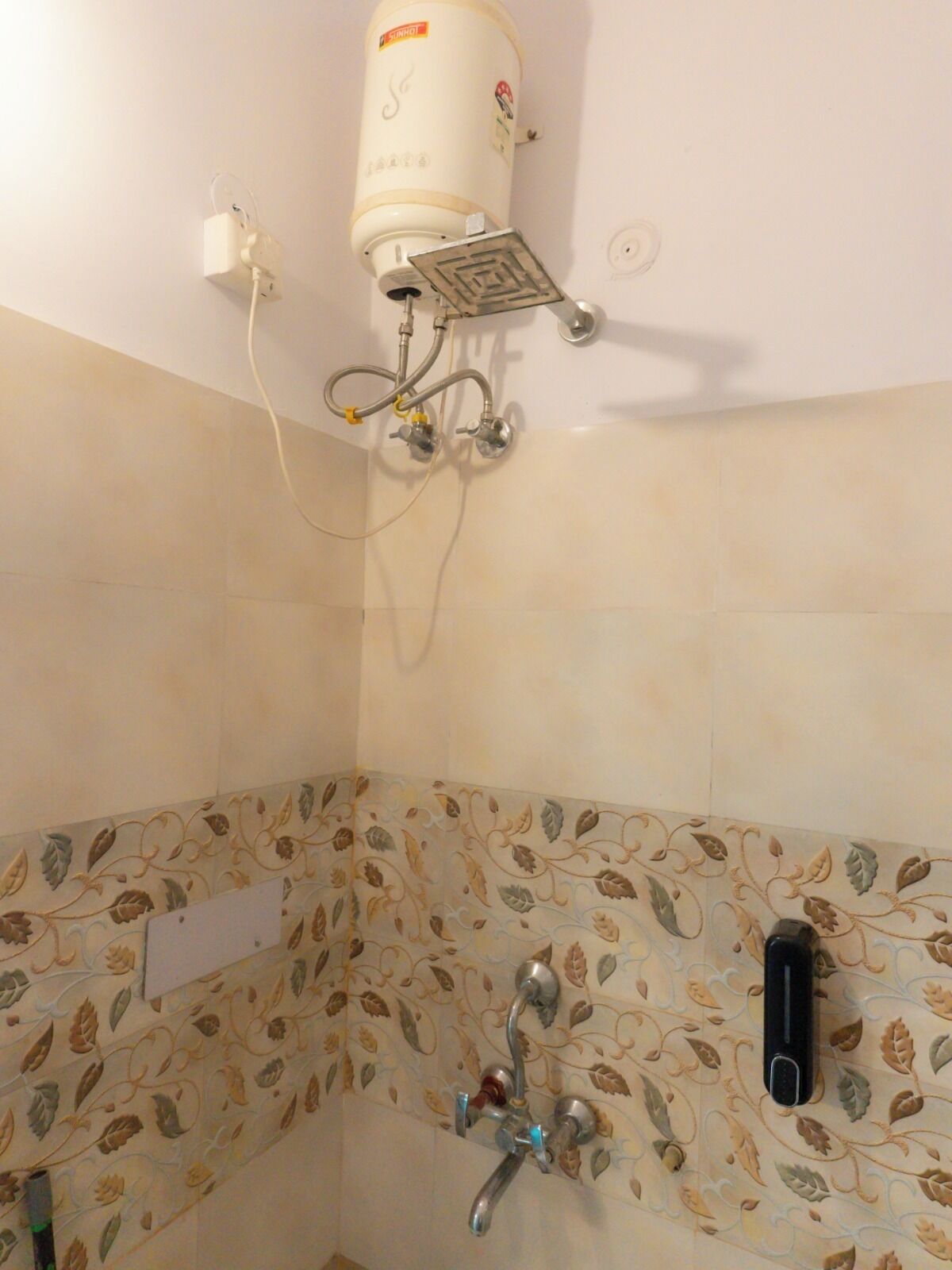 Ein Badezimmer mit an der Wand montiertem Warmwasserbereiter, einer Duschbrause und einem Wasserhahn.