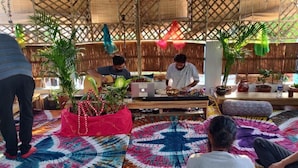 A room with a bamboo lattice ceiling, a central table with electronic equipment, and several potted plants. - The Pink Chapter Hostel, Jaipur (Jaipur)