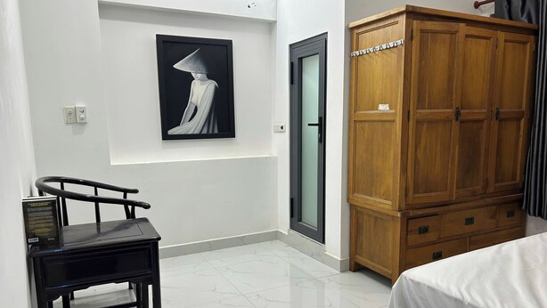 A hotel room with a bed, a wooden wardrobe, a framed artwork on the wall, and a desk with a chair. - T&M Homestay (Ho Chi Minh City)