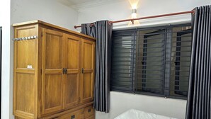A bedroom with a wooden wardrobe, a bed, and a window with curtains. - T&M Homestay (Ho Chi Minh City)