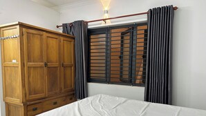 A bedroom with a wooden wardrobe, a window with blinds, and a bed with a white sheet. - T&M Homestay (Ho Chi Minh City)