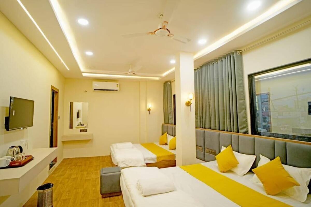 A hotel room with two beds, a TV, a desk, and a window with curtains.