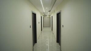 A long, narrow hallway with doors on both sides, recessed lighting on the ceiling, and a shiny tiled floor. - Avanti inn (Ujjain)