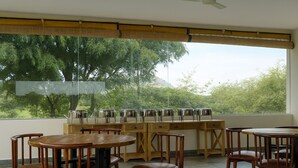 A room with a large window, a ceiling fan, and a wooden table with chairs. - Jawai Vanya Bagh - Luxury Leopard Safari Resort (Bali)