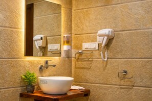 A bathroom with a large mirror, a hairdryer, a phone, a sink with a bowl, and a potted plant. - Jawai Vanya Bagh - Luxury Leopard Safari Resort (Bali)