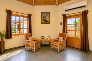 Una habitación con dos sillones de mimbre, una mesa con una tetera y un cuadro en la pared.
