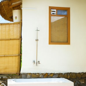 A bathroom with a bathtub, a window with blinds, and a bamboo fence.