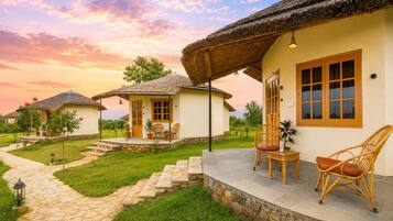 Una serie de casas rurales con techos de paja, senderos de piedra, mobiliario exterior y un cielo al atardecer.