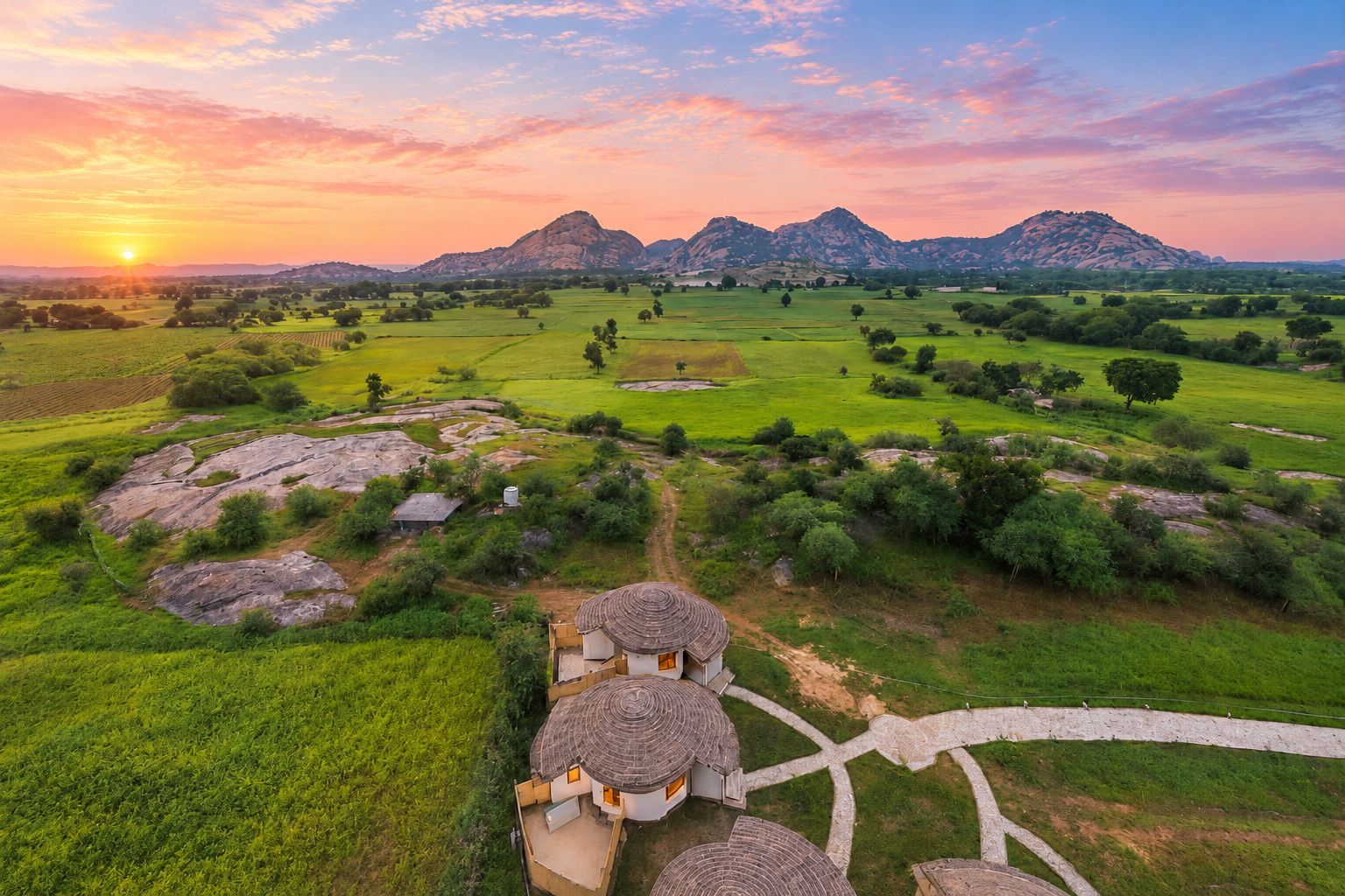 Paisagem rural com uma casa tradicional, campos abertos e montanhas ao fundo.