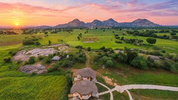 Paisagem rural com uma casa tradicional, campos abertos e montanhas ao fundo.