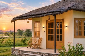 A house with a thatched roof, a porch with wicker chairs, and a view of the landscape.