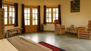A spacious room with a bed, two wicker chairs, a small table, and a painting on the wall. - Jawai Vanya Bagh - Luxury Leopard Safari Resort (Bali)