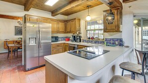 A kitchen with wooden cabinets, a stainless steel refrigerator, a large island with a built-in stove, and a hanging light fixture. - Gorgeous Adobe Home: Classic Santa Fe Style in ABQ (Albuquerque)