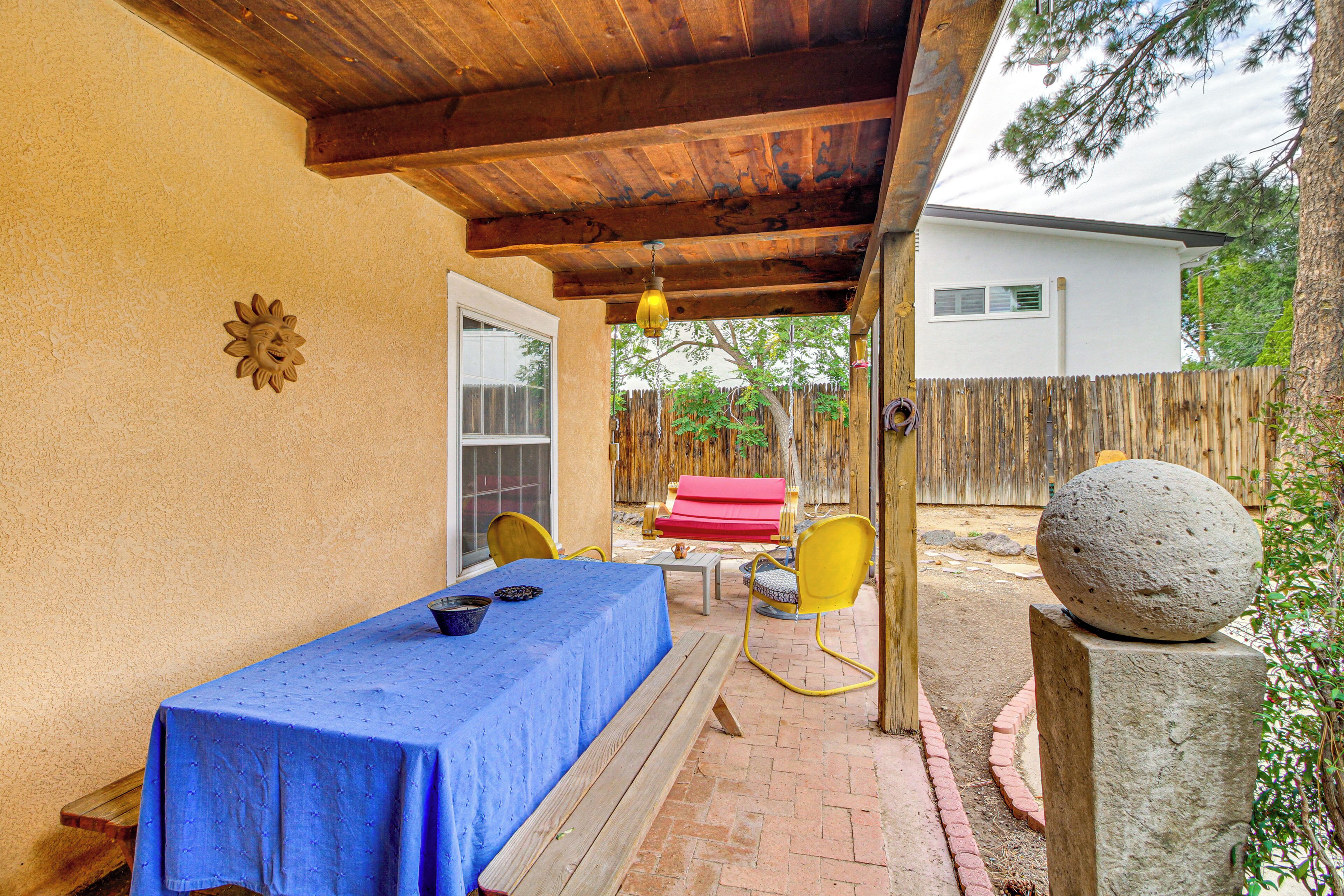 An outdoor patio with a table covered in a blue tablecloth, yellow chairs, and a stone ball on a pedestal.