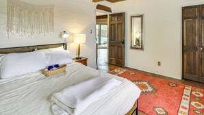 A bedroom with a large bed, a bedside lamp, a woven basket, a patterned rug, and a wooden door. - Gorgeous Adobe Home: Classic Santa Fe Style in ABQ (Albuquerque)