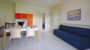 Un salon moderne avec un canapé bleu, une table à manger avec des chaises et un coin cuisine doté de meubles rouges.