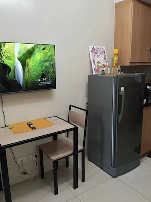 Uma pequena cozinha compacta equipada com geladeira, micro-ondas e televisão de tela plana fixada na parede.