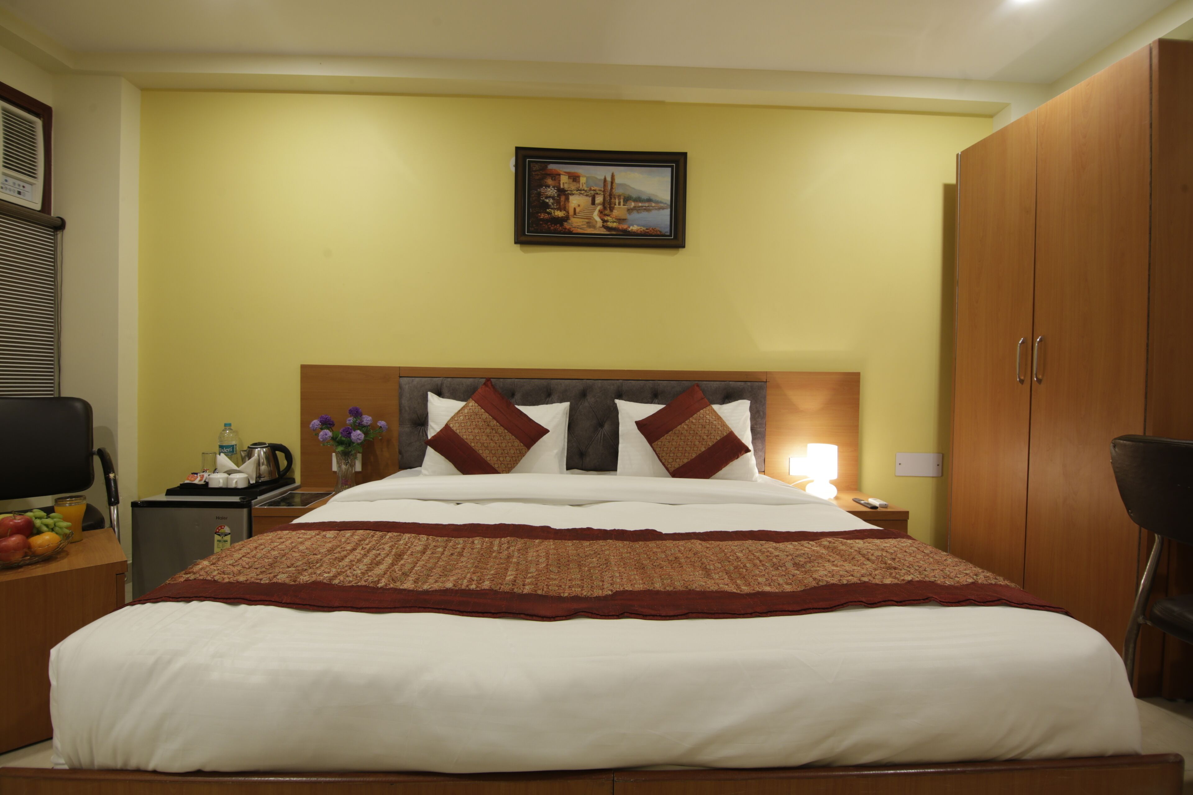 Une chambre d’hôtel avec un grand lit, une table de chevet avec une lampe, un petit bureau avec un ordinateur, une chaise et une armoire.