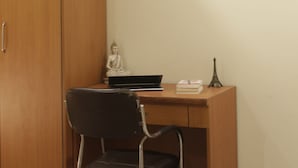 A room with a wooden wardrobe, a desk with a laptop, a chair, a Buddha statue, and a framed picture on the wall. - Hotel TMS Grand (New Delhi)