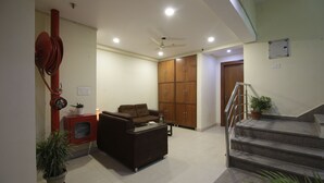 A living room with a sofa, coffee table, and potted plants. There is a staircase leading to another level. - Hotel TMS Grand (New Delhi)