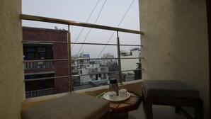 A balcony with a view of buildings, a table with a tray, a thermos, and a chair. - Hotel TMS Grand (New Delhi)