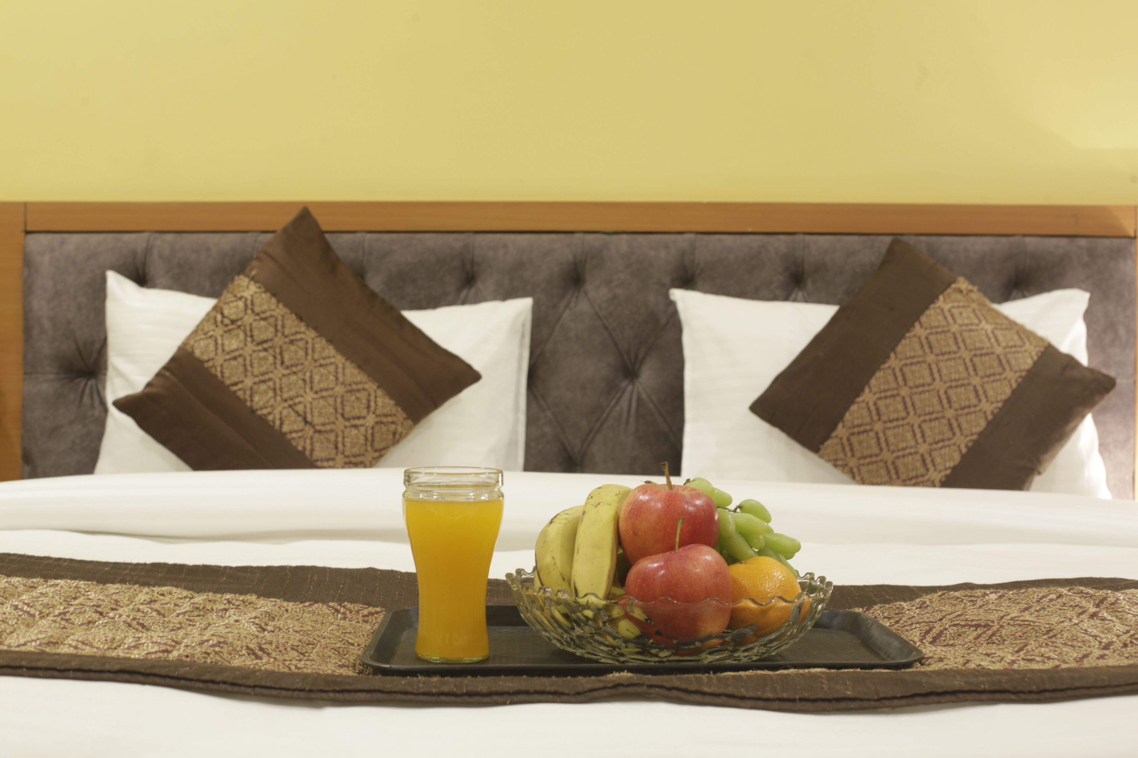 A neatly made bed with a tray of fruit and a glass of orange juice.