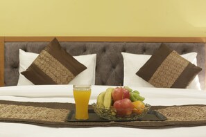 A neatly made bed with a tray of fruit and a glass of orange juice. - Hotel TMS Grand (New Delhi)