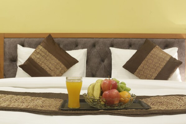 A neatly made bed with a tray of fruit and a glass of orange juice.