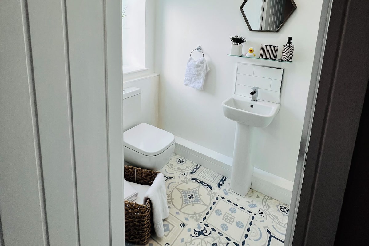 A bathroom with a toilet, sink, and mirror. There is a towel hanging on the wall and a basket on the floor.