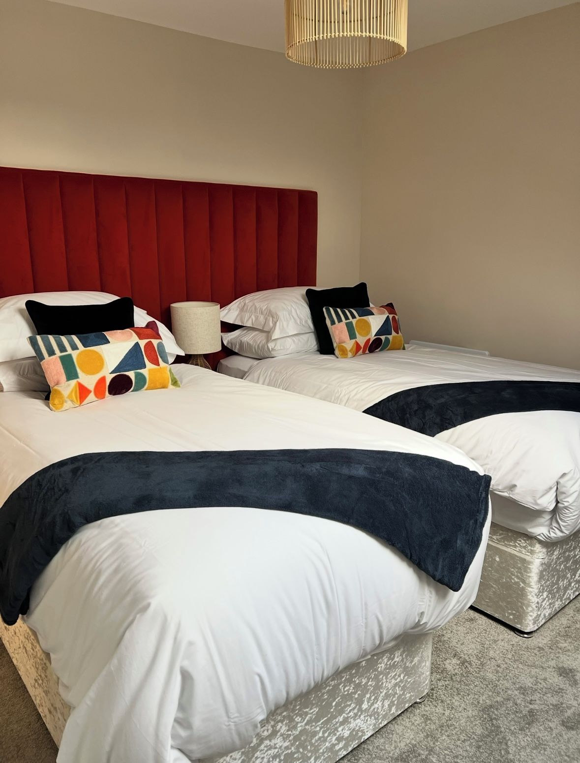 Habitación de hotel con dos camas, cabecero rojo y lámpara colgante.