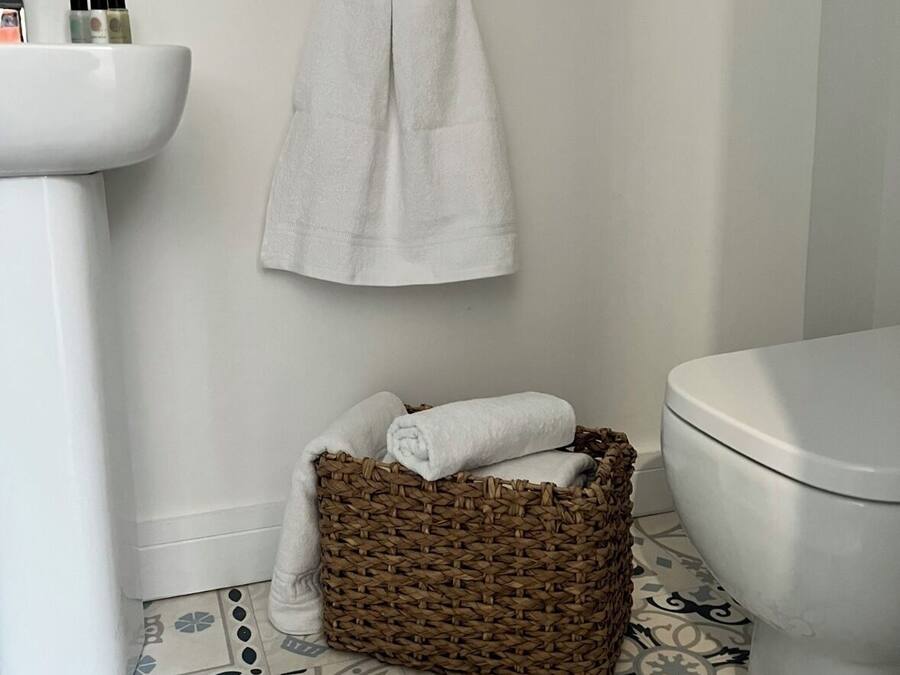 A bathroom with a white sink, a toilet, a woven basket with towels, and a patterned floor.
