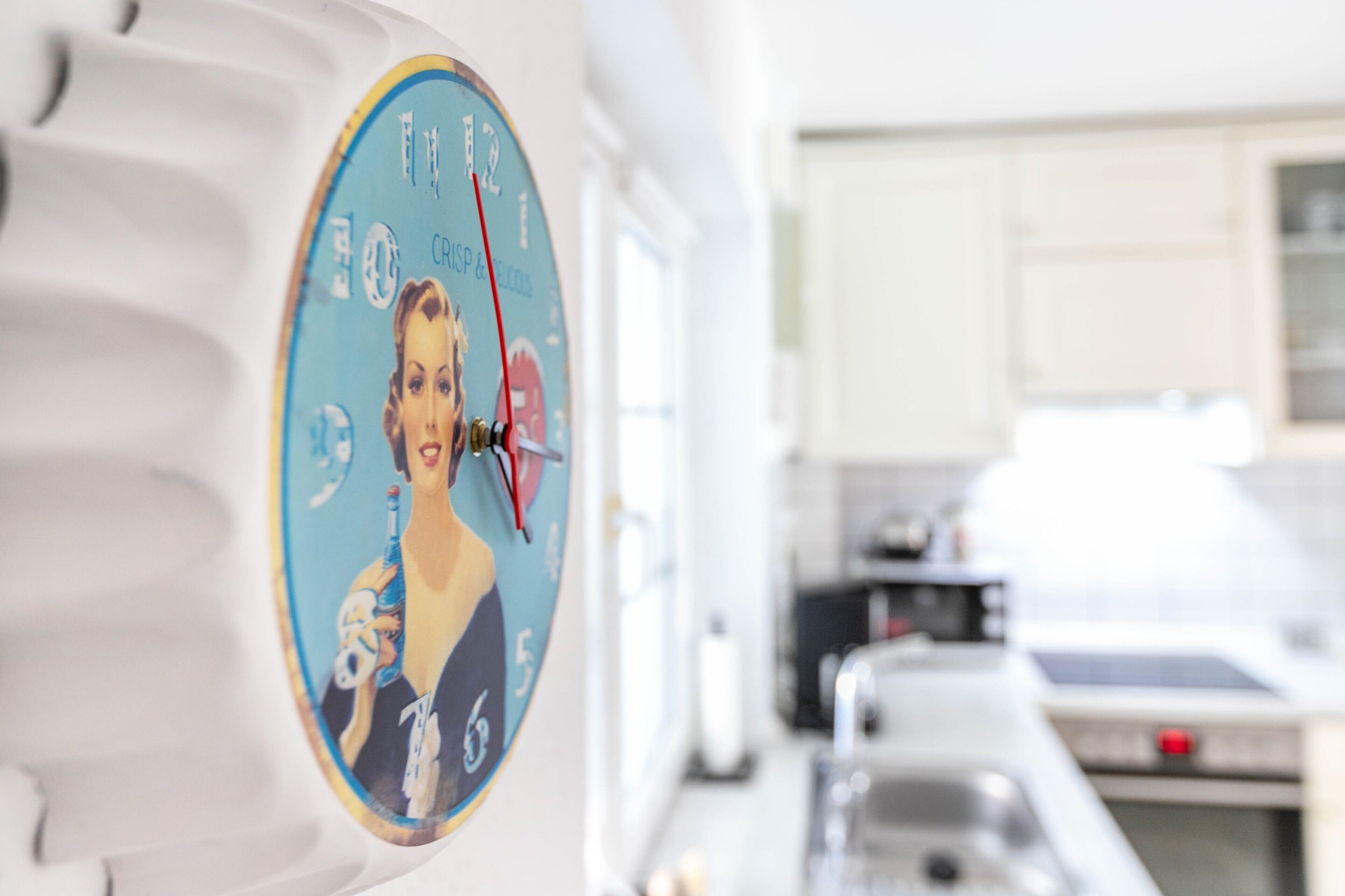 Une cuisine avec des meubles blancs, une horloge au design rétro et un évier.