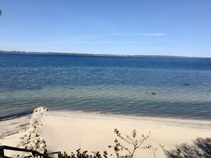Ein Strand mit klarem Wasser, sandigem Ufer und einer entfernten Küste.